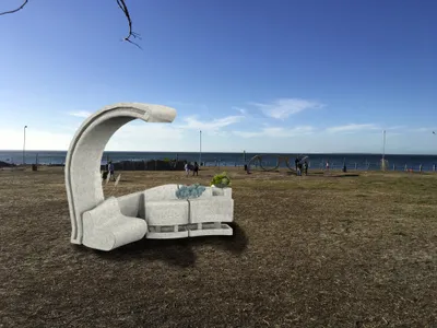 This image showcases a contemporary concrete sculpture set in an open, coastal landscape. The sculpt