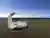 This image showcases a contemporary concrete sculpture set in an open, coastal landscape. The sculpt