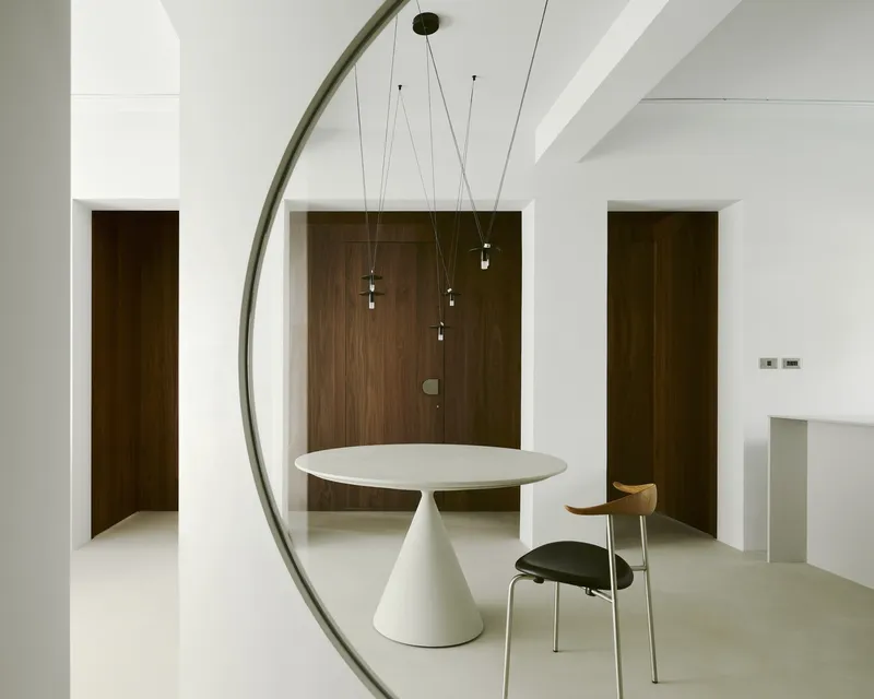 View through freestanding circular mirror frame toward walnut doors and white archway beyond