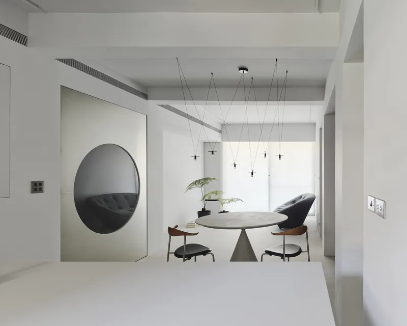 Dining table with conical pedestal base framed by large circular mirror reflecting shelves beyond