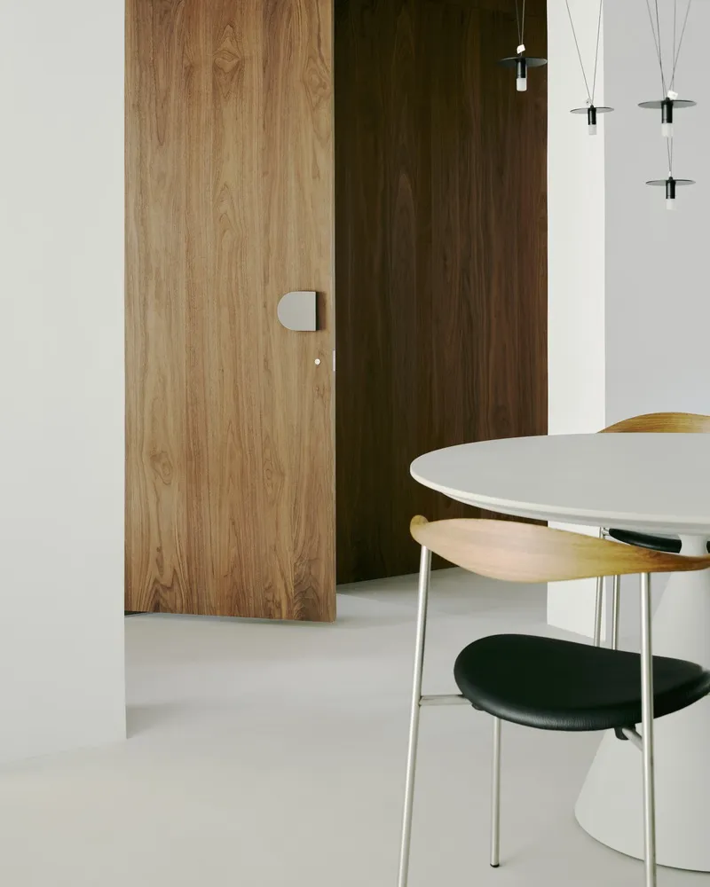 Close-up of walnut veneer door panels beside white dining table with wire pendant fixtures overhead