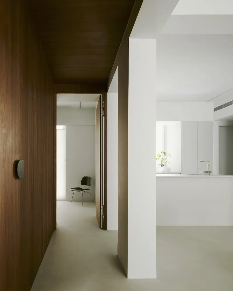 Corridor with wood-paneled wall and ceiling alongside white volumes and grey polished floors