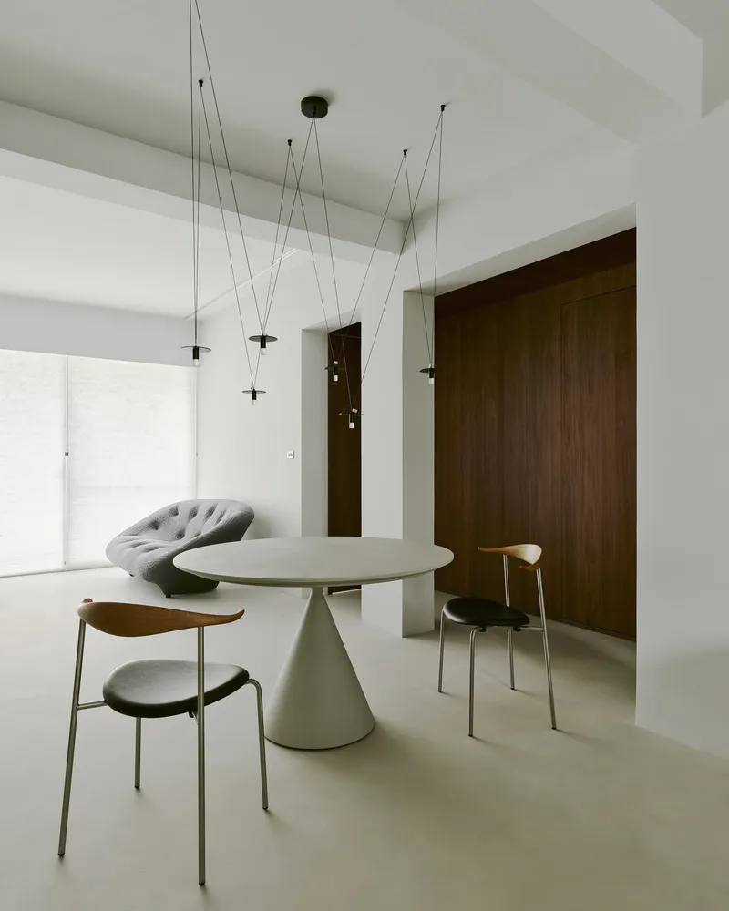 Dining area with conical table base and suspended light fixtures beneath coffered white ceiling