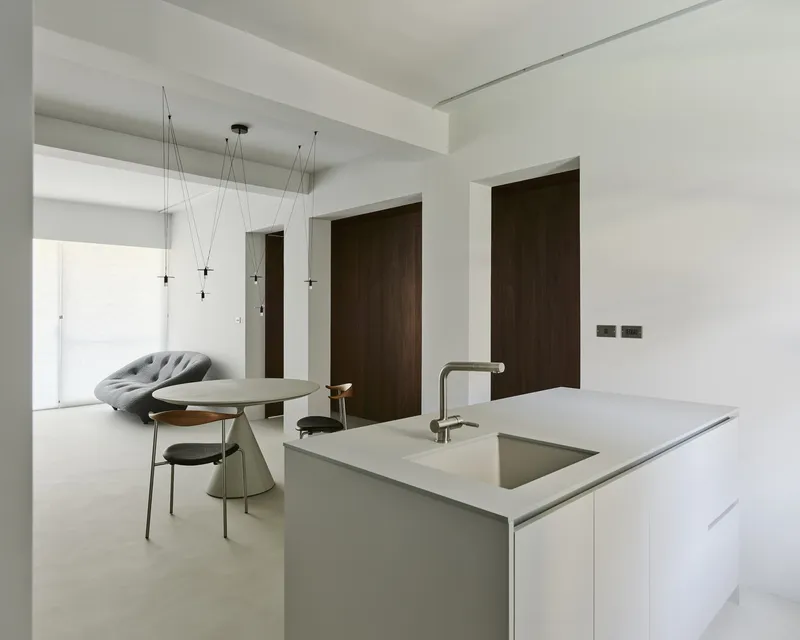 Open kitchen with pale stone island and integrated sink facing a dining area with dark timber doors