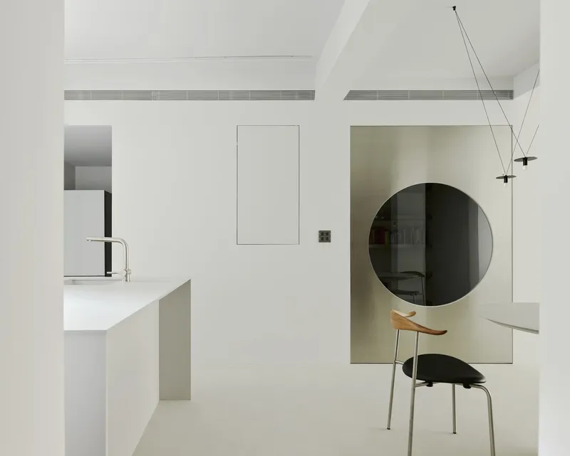 White wall partition with a large circular tinted mirror reflecting a built-in bookshelf and desk chair