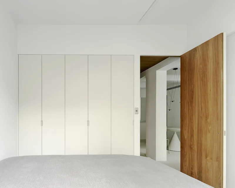 Bedroom with flush white wardrobe wall and timber door opening to adjacent living space
