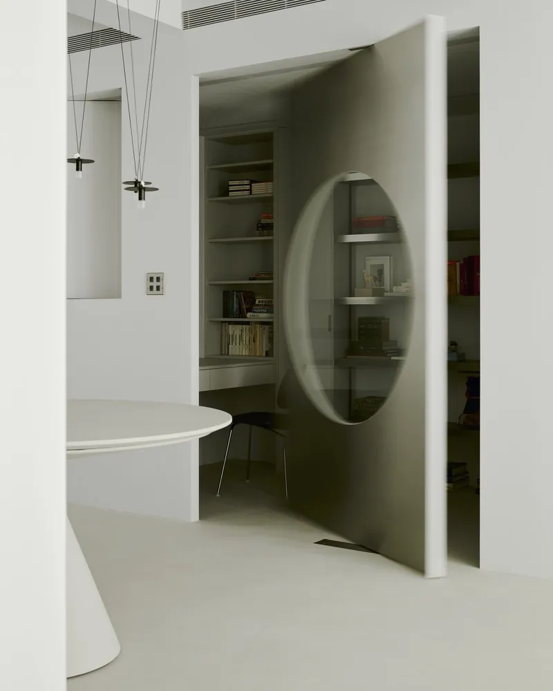 Angled view through a circular portal opening revealing built-in shelving with books and wire pendant lights