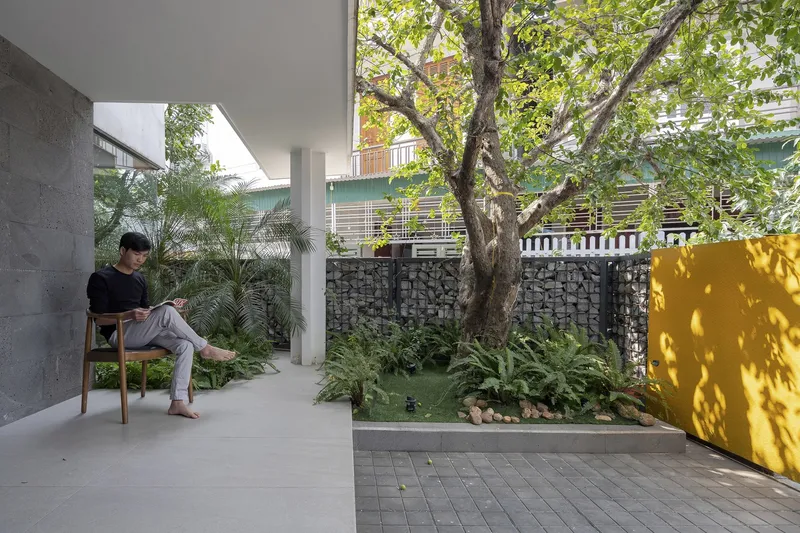 Covered terrace with a person seated beside a garden bed and gabion wall