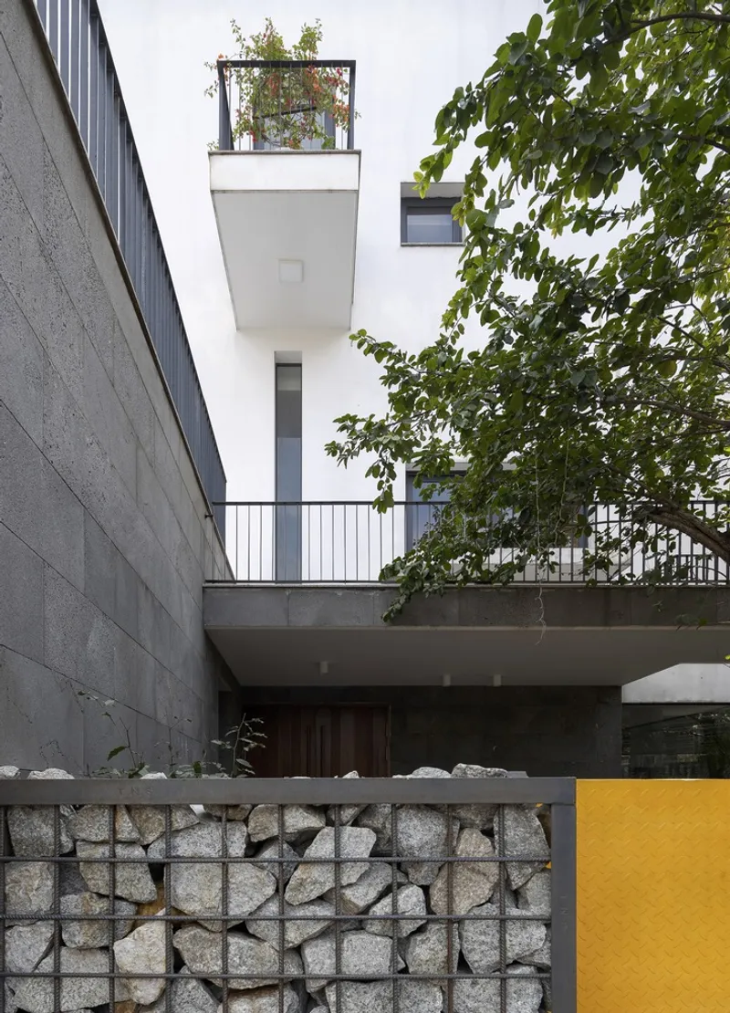 Gabion wall with yellow panel beside concrete terraces and a planted rooftop balcony