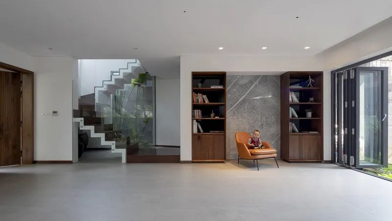 Open interior with dark timber staircase behind glass and a person seated in an orange chair