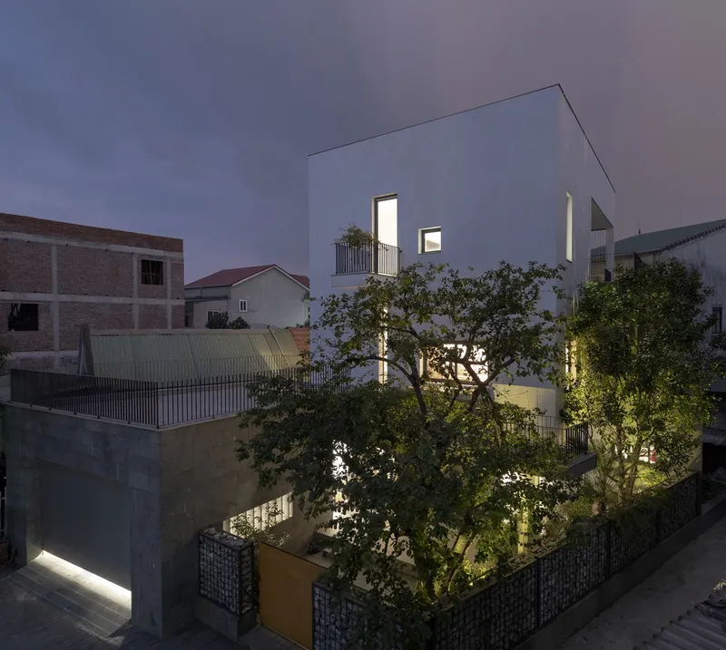 Rear view of white rendered volumes and terraces surrounded by trees at twilight