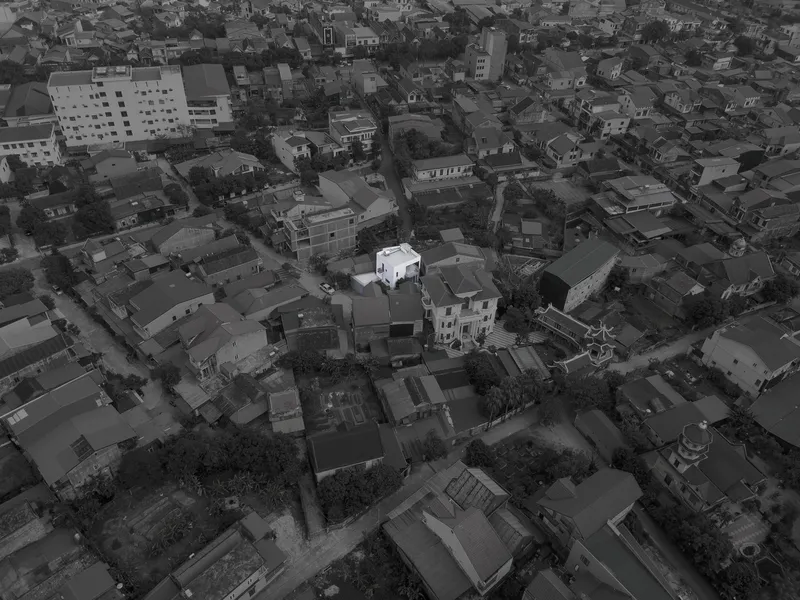 Aerial view of a white cubic residence nestled among densely packed rooftops in a residential neighborhood