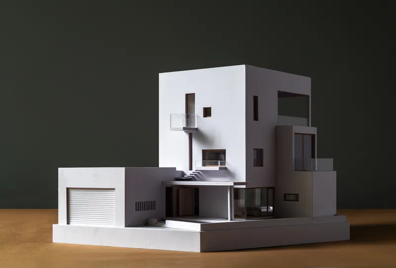 Physical model showing interlocking volumes with punched windows and a garage door photographed against dark backdrop