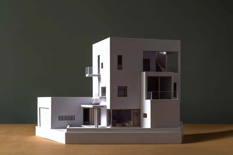 Physical model with illuminated interior revealing staircase and spatial layering through cut openings
