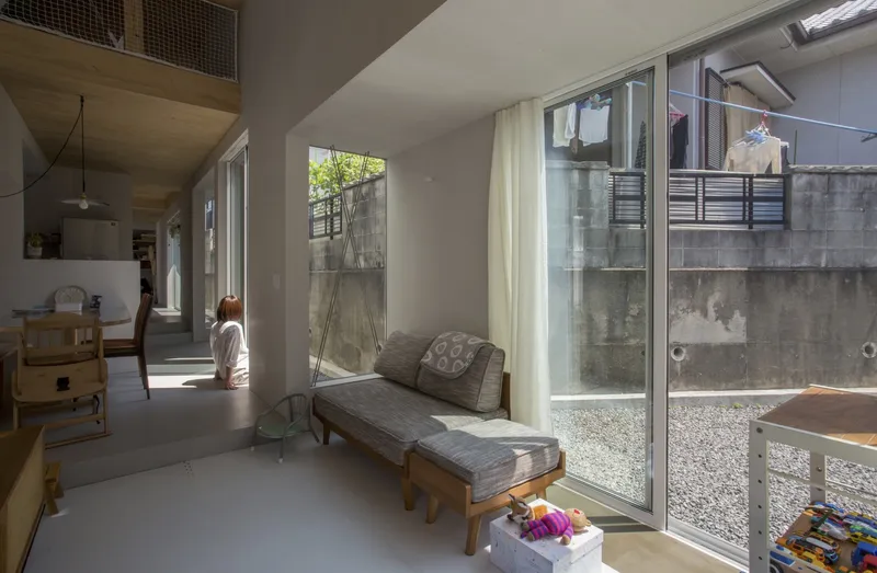Living area with timber daybed facing a glazed courtyard with concrete walls and gravel ground