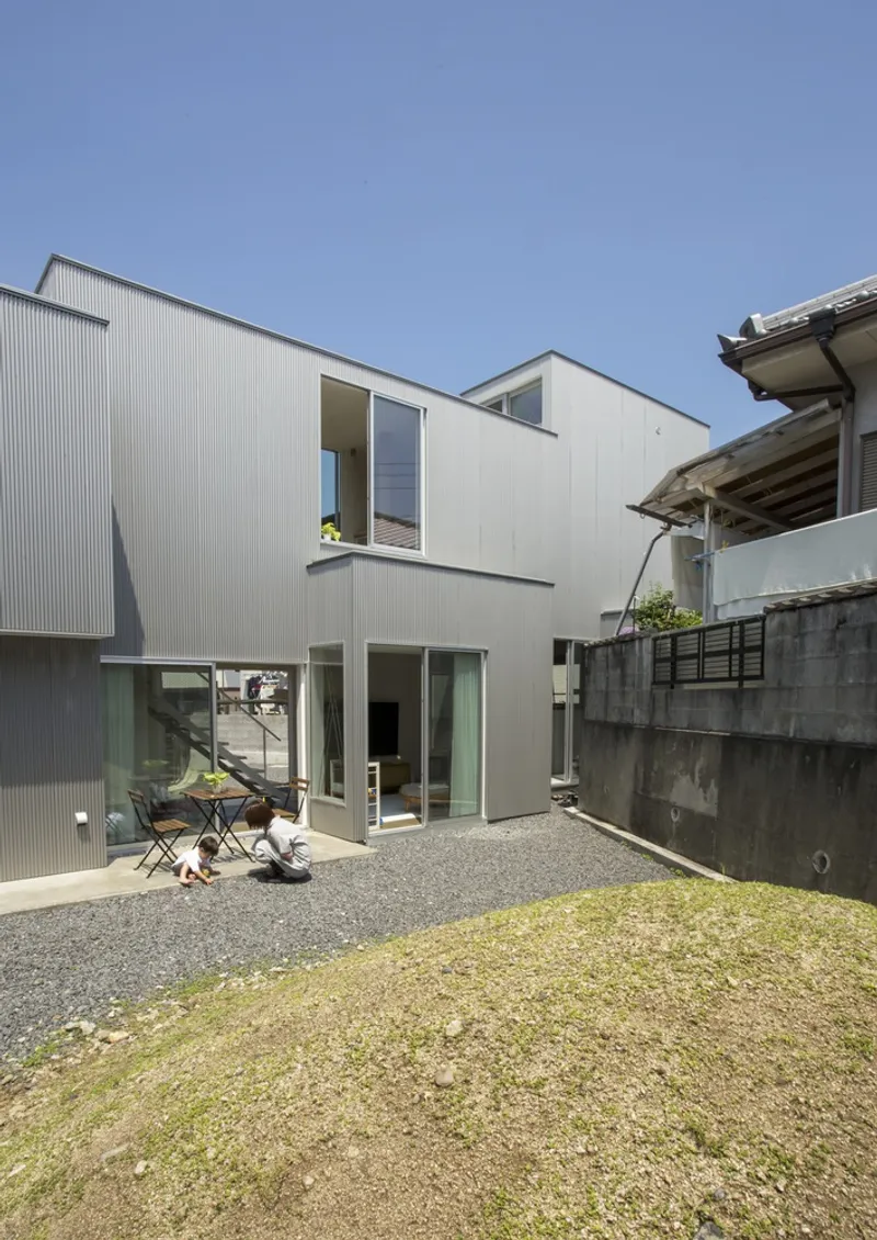 Rear courtyard with stepped white volumes and gravel ground adjacent to a patch of grass