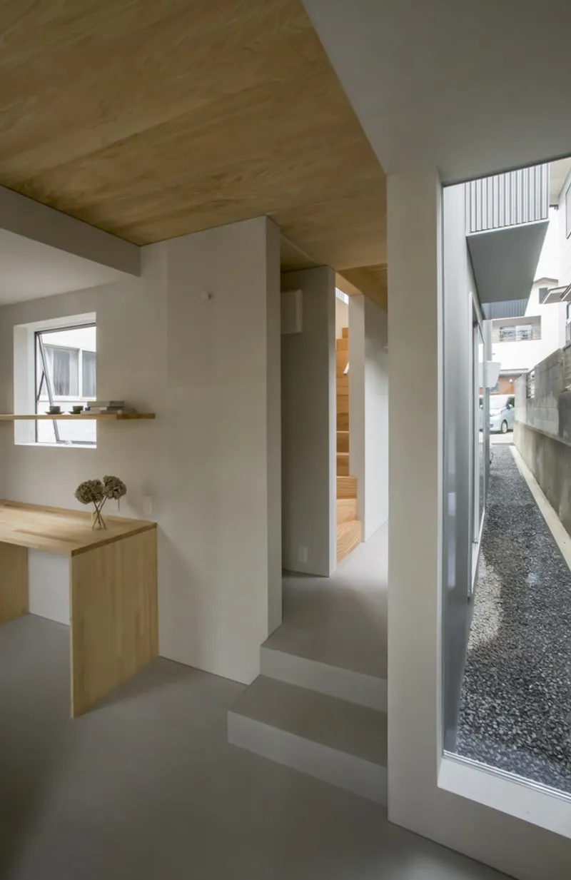 Split-level interior with concrete steps descending past a timber desk toward a gravel courtyard