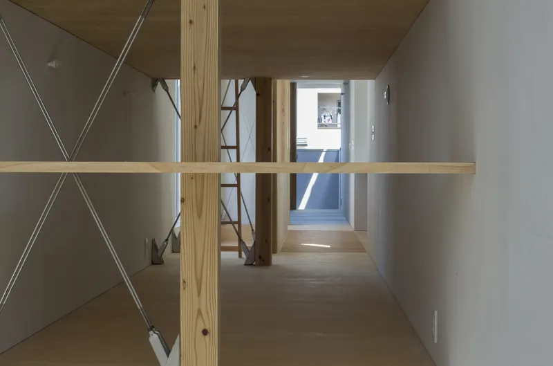 View through an interior bridge with timber floor and exposed columns into daylit corridor beyond