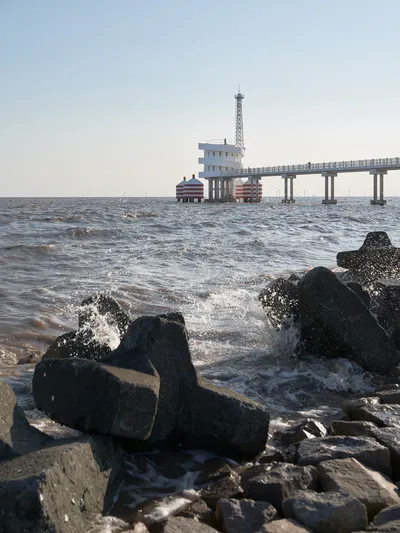 This architectural image showcases a coastal scene featuring a pier with an observation tower extend