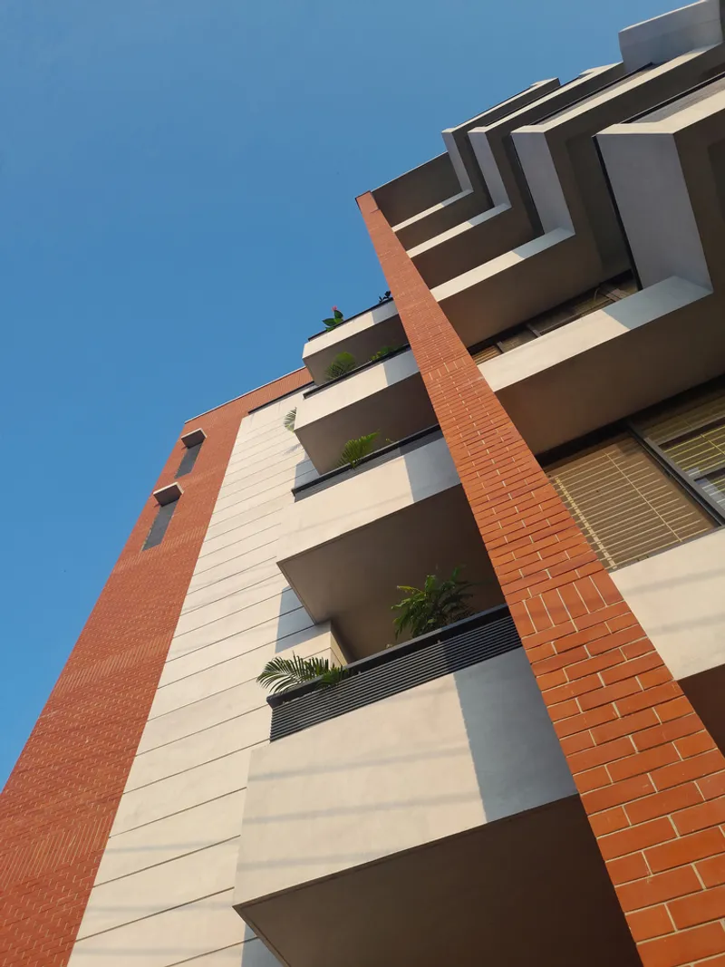 Upward view of stacked balconies with terracotta brick fins and planted greenery against blue sky