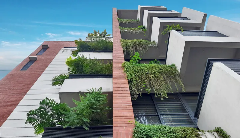 Facade showing recessed balconies with cascading planting and vertical brick louvers under daylight