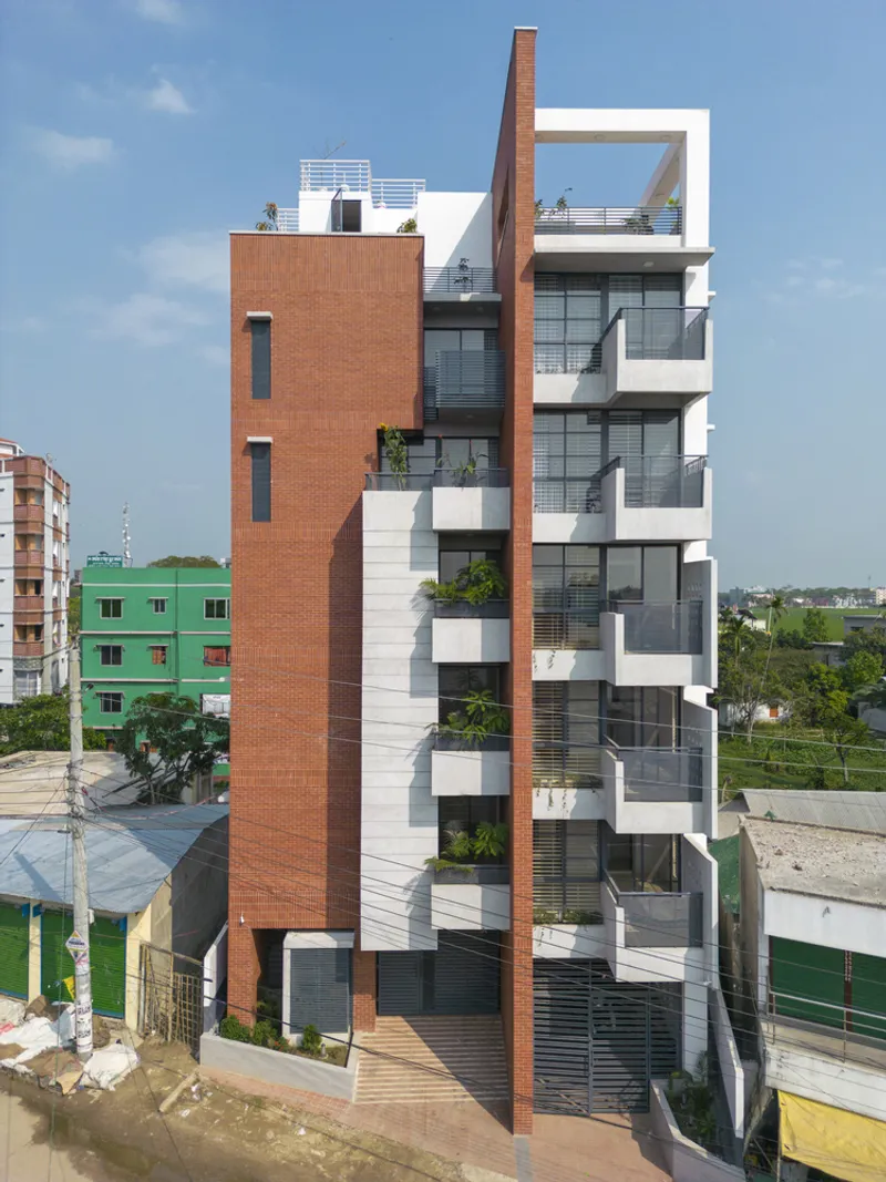 Multi-story residential tower with brick fins and planted balconies in a dense neighborhood