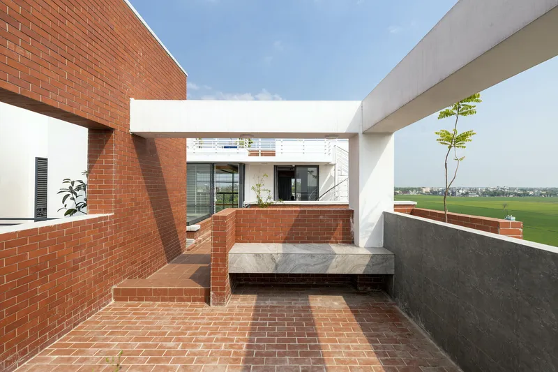 Roof terrace with red brick paving, concrete bench, and planted sapling overlooking agricultural fields
