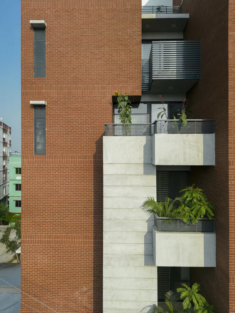 Staggered concrete balconies with metal railings and plantings between brick facade volumes under clear sky
