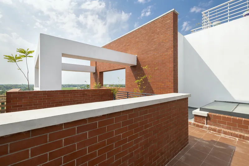 Rooftop terrace with brick parapet walls and framed openings overlooking distant green landscape under cloudy sky