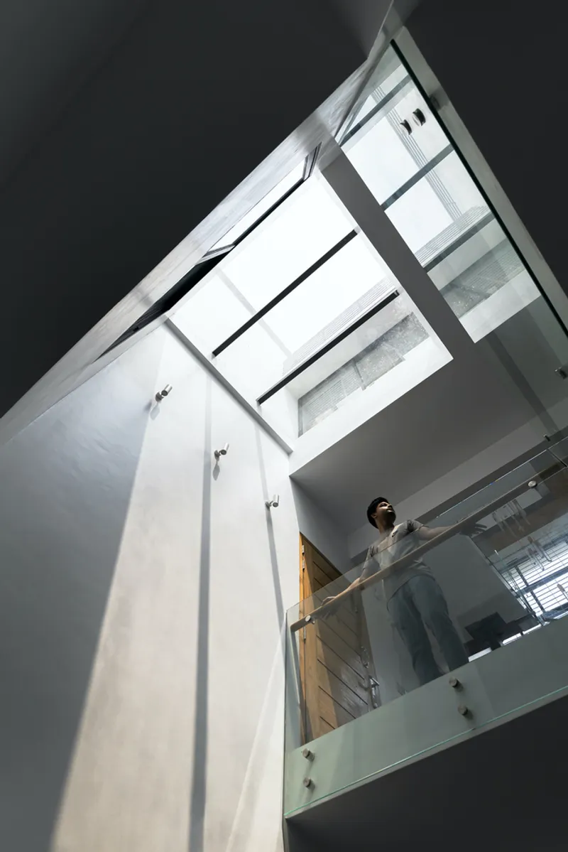 View up the stairwell toward a skylight with a figure standing at the timber-clad landing above