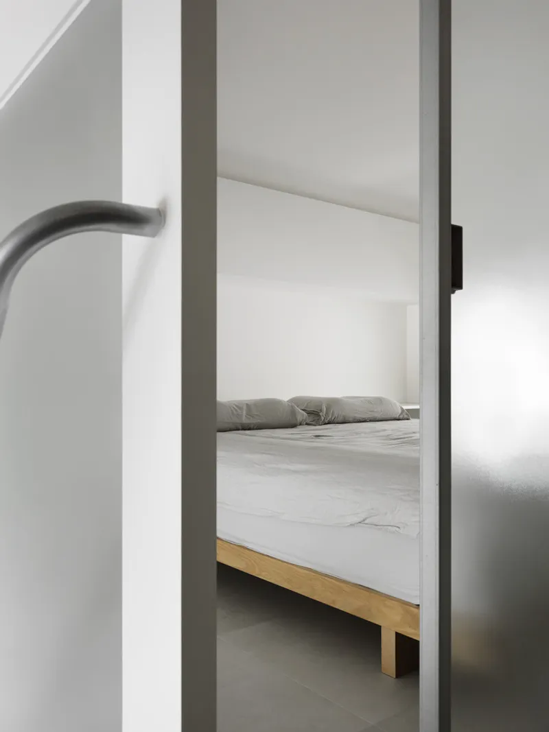 Framed view through a doorway to a timber bed in a white-walled bedroom