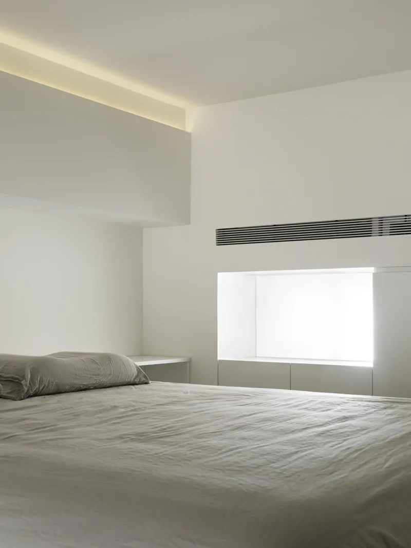 Bedroom corner with recessed ceiling cove lighting and horizontal air conditioning vent above a window