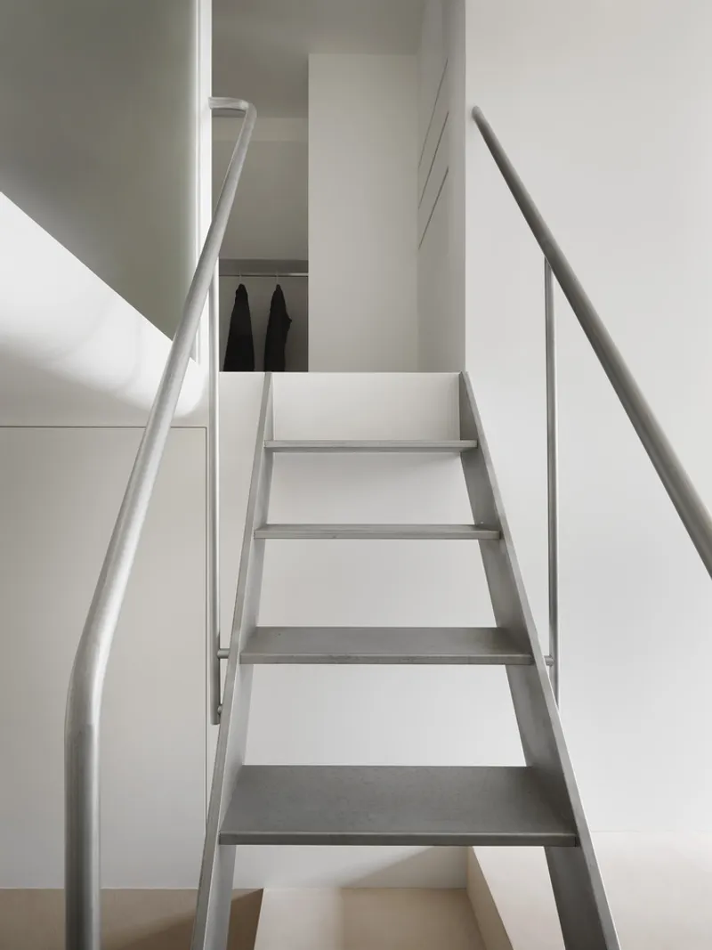 White steel staircase with open risers ascending between curved walls under natural daylight