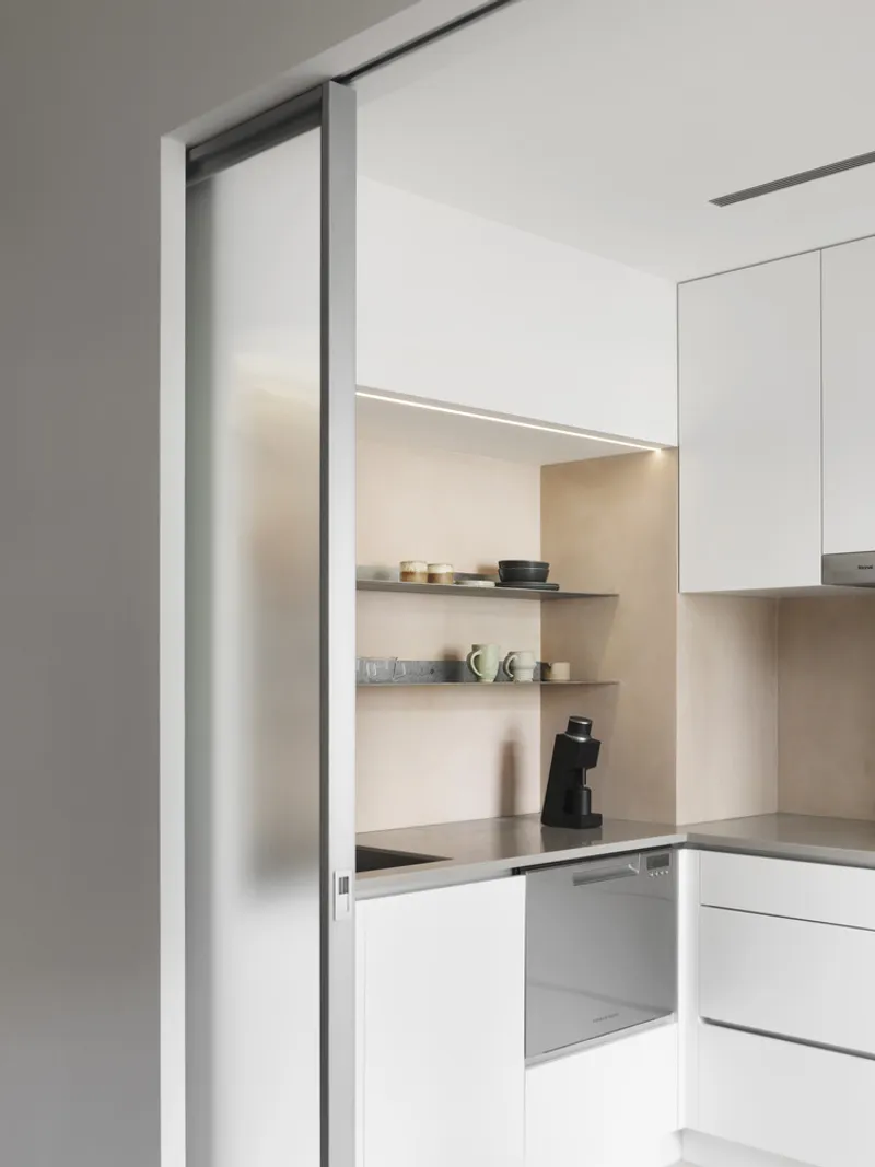 Kitchen alcove with sliding frosted glass panel revealing lit open shelving and grey countertops