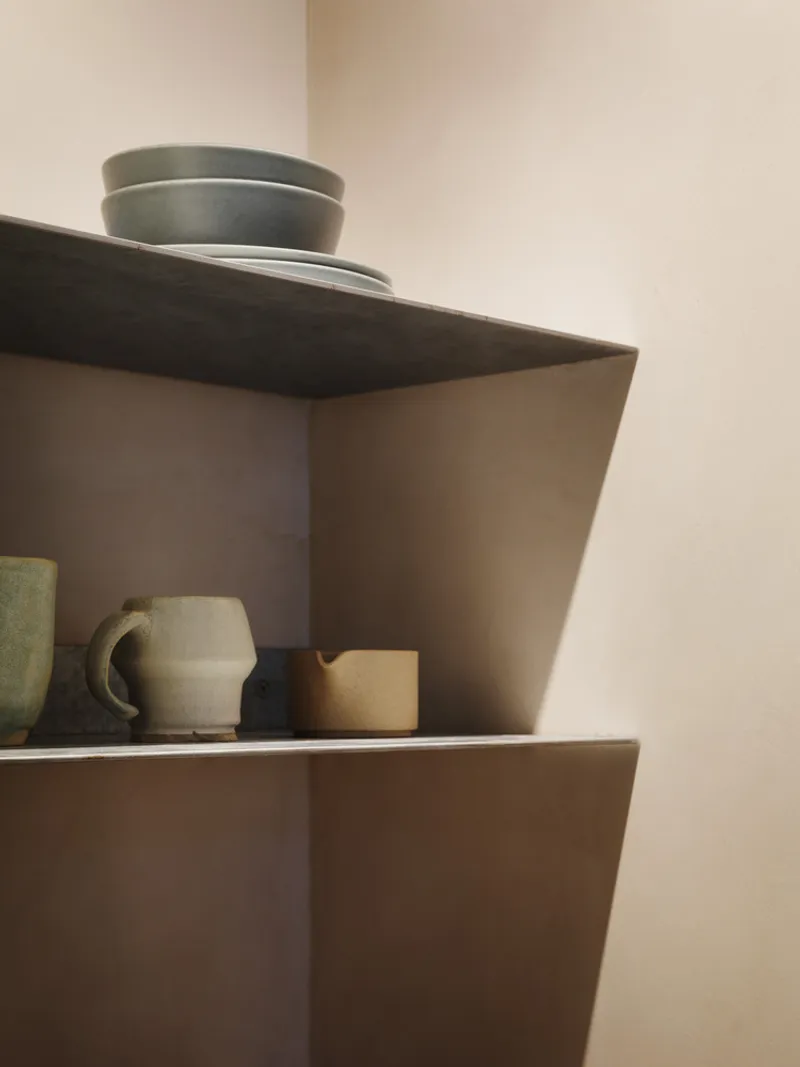 Corner detail of cantilevered timber shelves holding ceramic bowls and cups in afternoon light