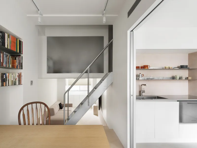 Dining area with oak table looking past steel staircase toward white kitchen under track lighting
