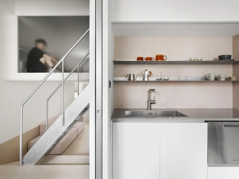 White kitchen niche with stainless steel counter and open shelving displaying ceramic cups and glassware
