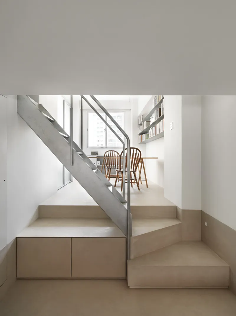 Timber staircase with integrated storage drawers rising toward dining area with wooden chairs