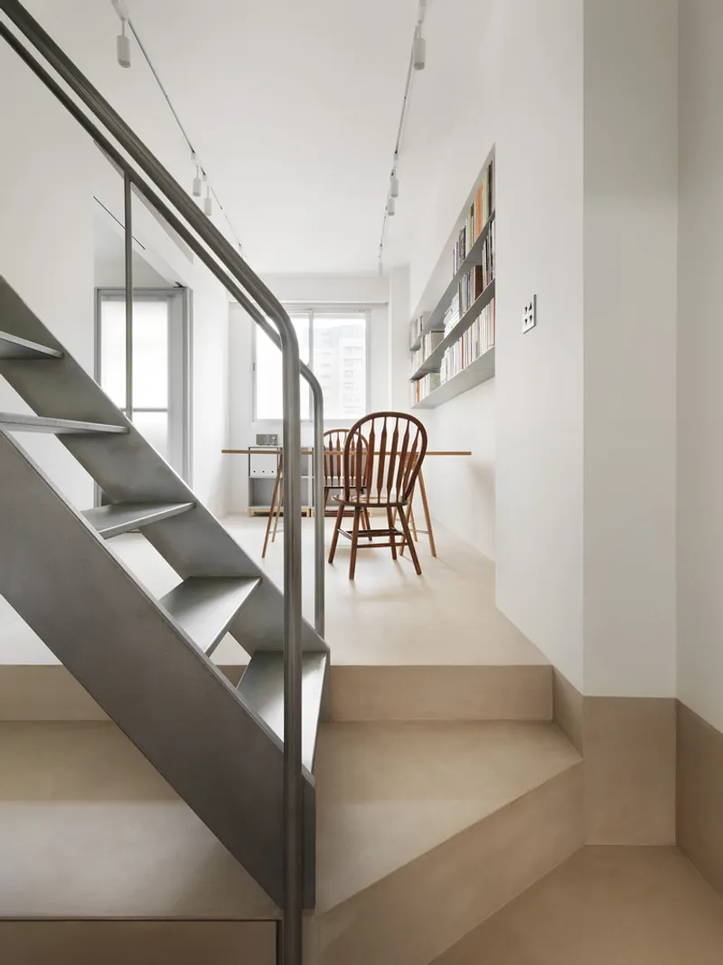 Steel staircase with open treads rising past built-in desk with bentwood chairs and shelving