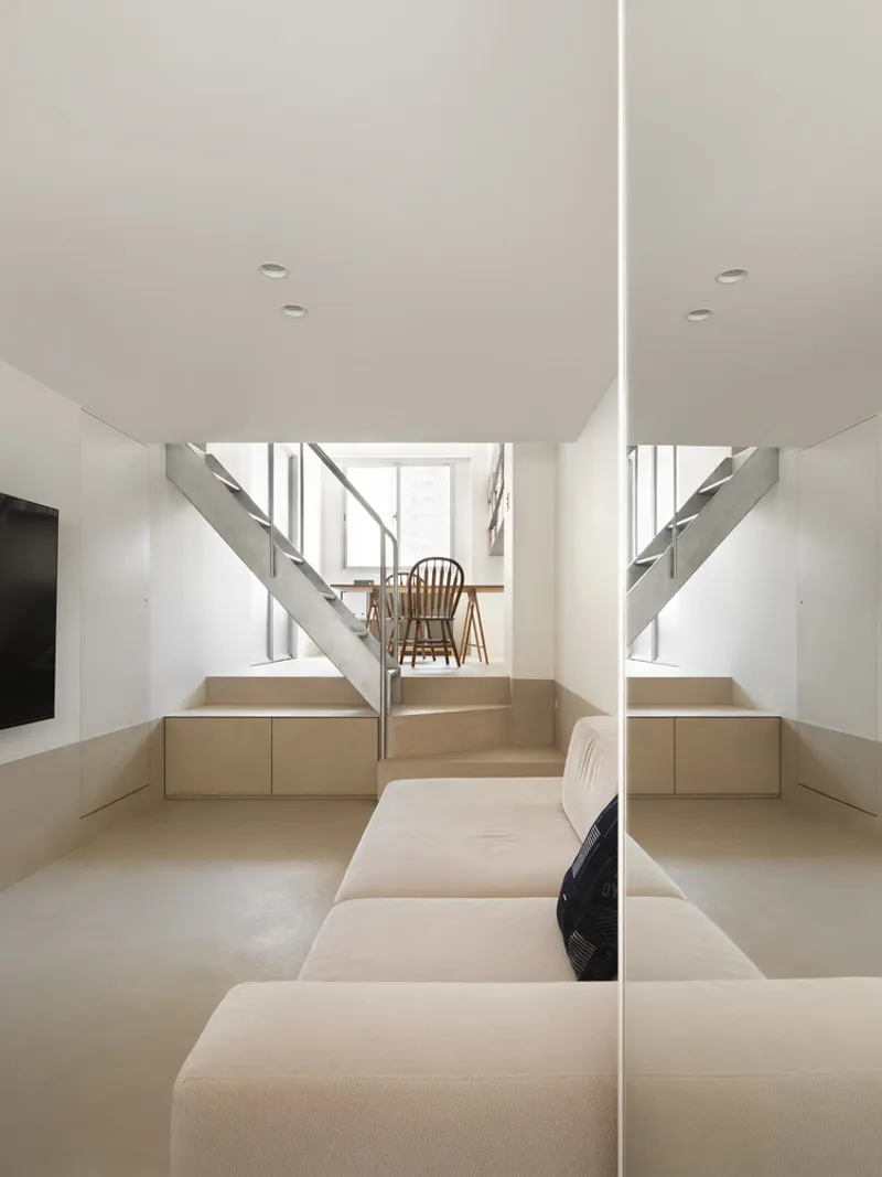 Double-height space with mirrored steel stairs flanking plywood built-in seating and storage platforms