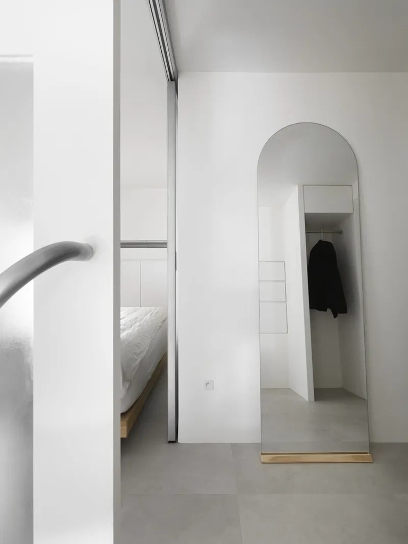 Arched mirror leaning against white wall revealing bedroom beyond open sliding partition