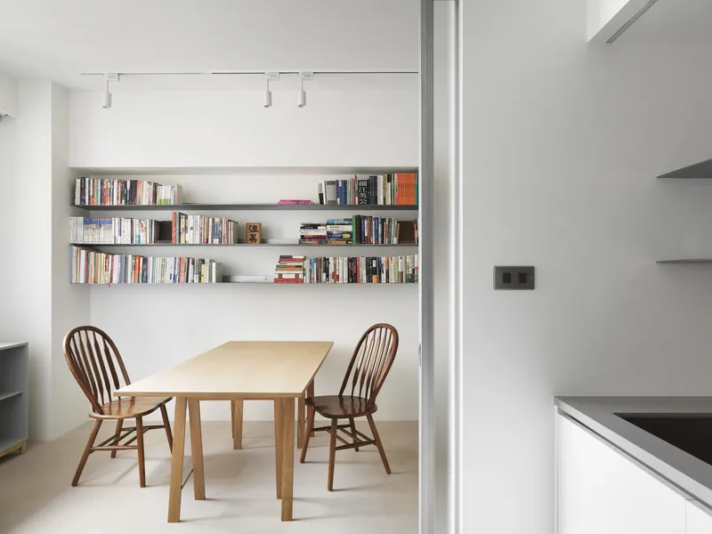 Dining area with timber table and Windsor chairs beneath wall-mounted shelving filled with books