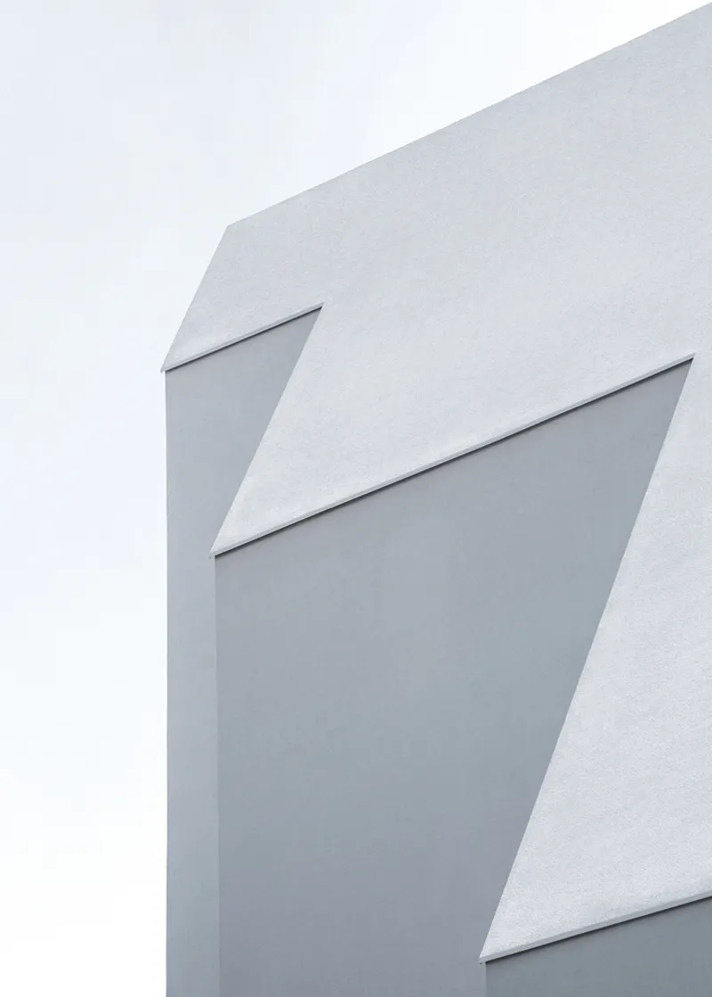 Close-up of white faceted facade with angular recesses against an overcast sky
