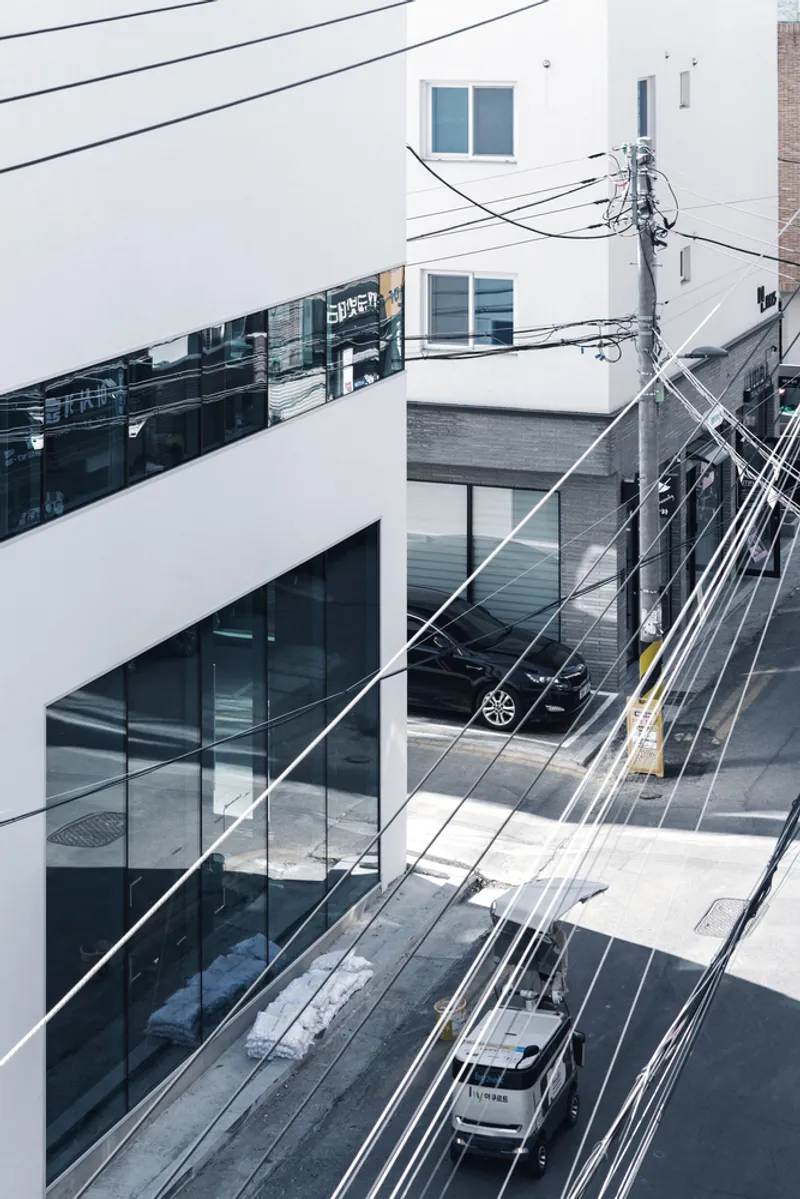 Oblique view showing the horizontal ribbon window wrapping the white facade above the wet street