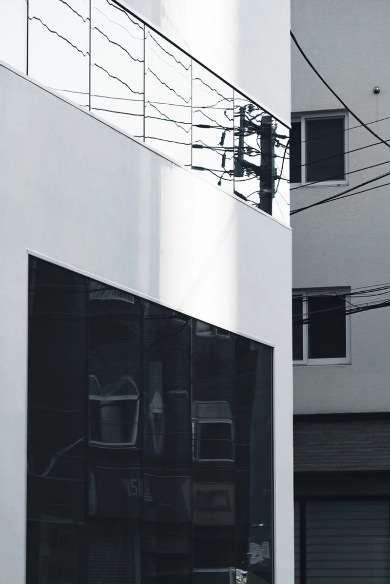 Close-up of the white facade planes with dark glass openings and utility wires crossing overhead