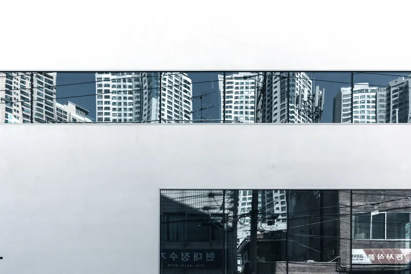 White facade with continuous horizontal ribbon window showing reflections of surrounding high-rise towers