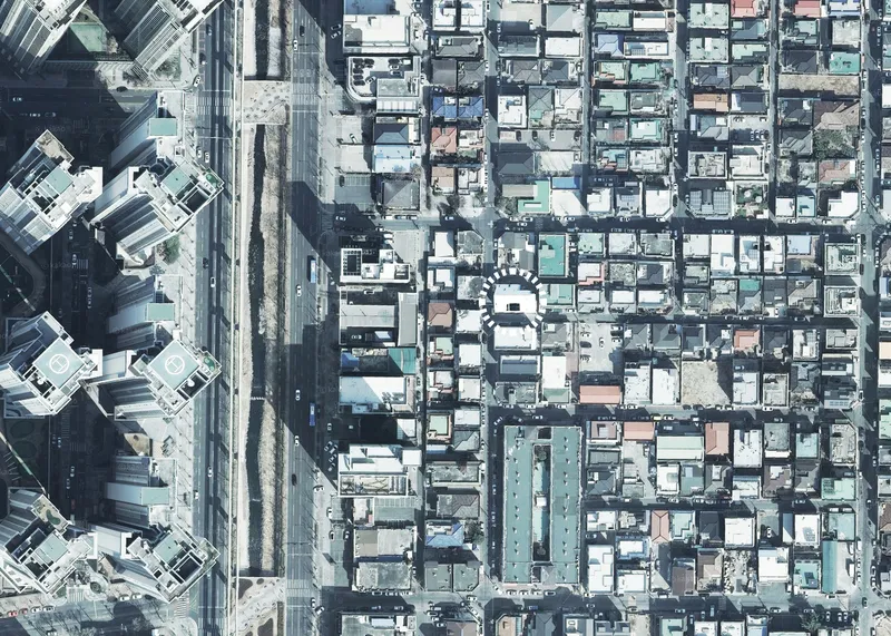 Aerial view showing white angled rooftop inserted within dense gridded neighborhood adjacent to rail corridor
