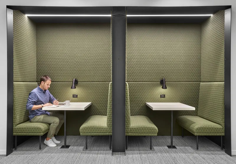 Twin work booths with olive green upholstered banquettes and white tables separated by a dark partition