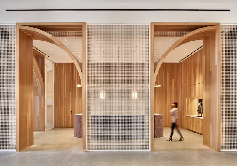 Symmetrical entrance with arched timber portals flanking a central mesh screen as a person walks through