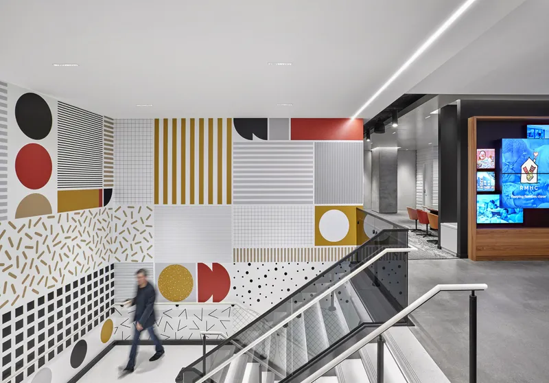 Graphic wall installation with geometric patterns in red, gold, and black beside a steel and glass staircase